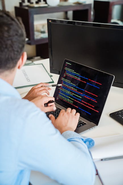 A close-up view of a computer screen displaying lines of source code in multiple colours, including red, blue, green, yellow, and white, with a blurred background. The code contains various programmin